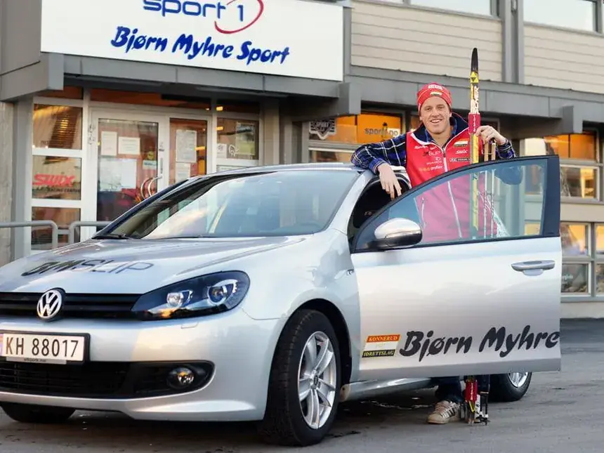 Butikken i Krokstadelva med Sport 1-skilt, og en firmabil med Bjørn Myhre-logo foran