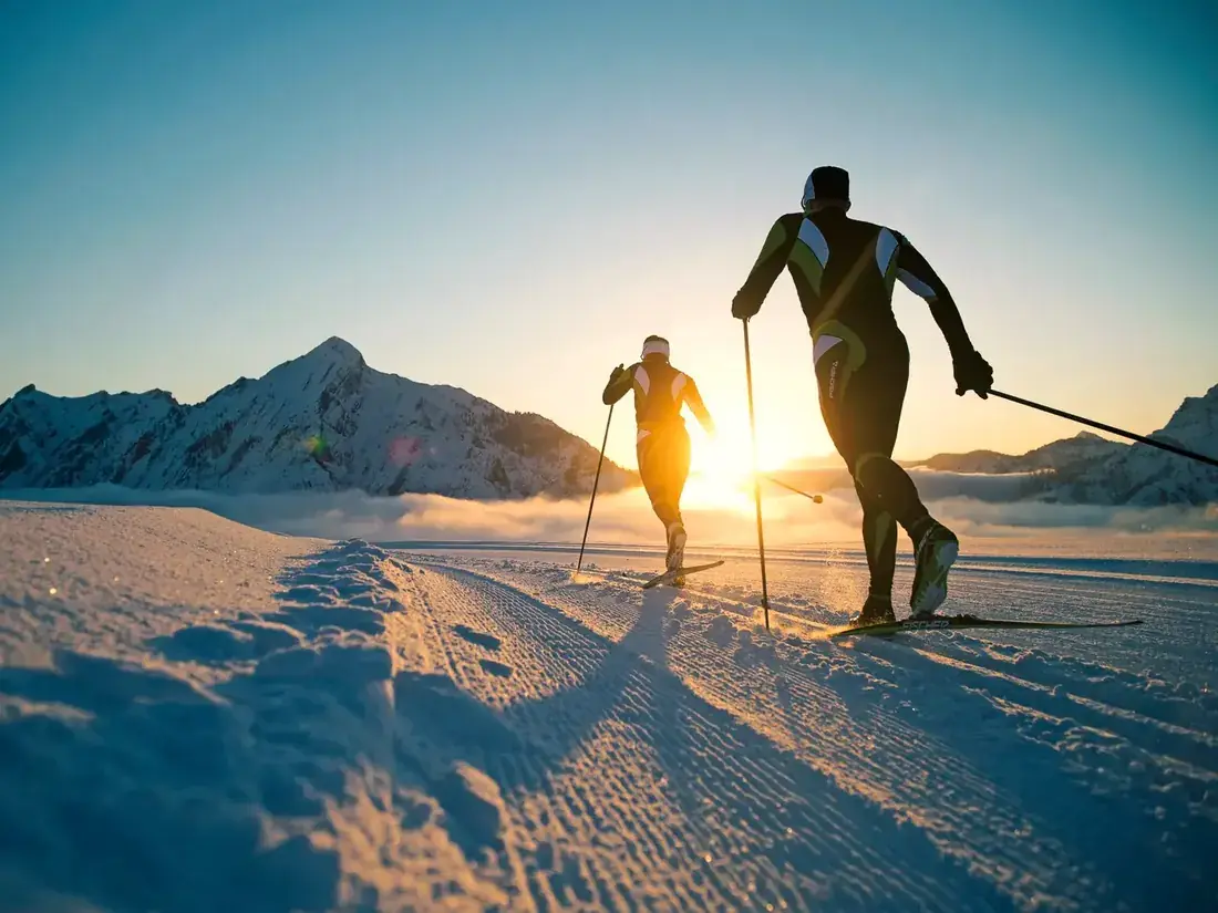 To skiløpere i motlys på et preparert spor i fjellet