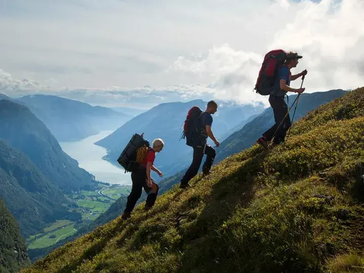 Tre turgåere med sekk i en bratt fjellside over en fjord